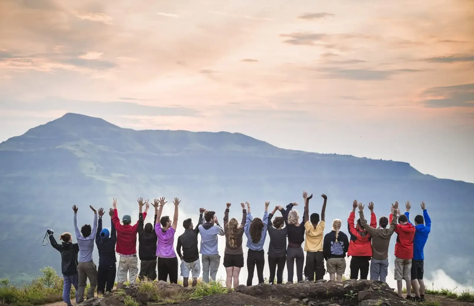 Students with arms raised on a hilltop at sunset